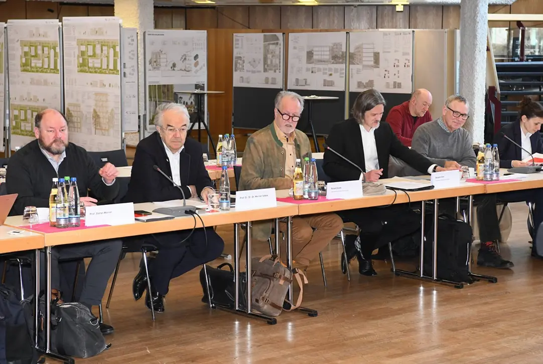 Expertengremium bei der KaepseLE-Jurysitzung an einem langen Tisch, im Hintergrund Architekturentwürfe