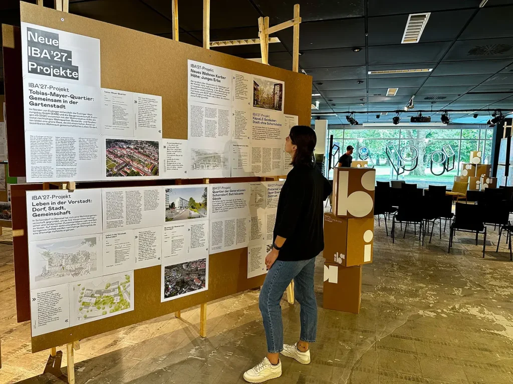 Person steht vor IBA'27-Projektausstellung mit mehreren Infotafeln zu neuen Stadtentwicklungsprojekten