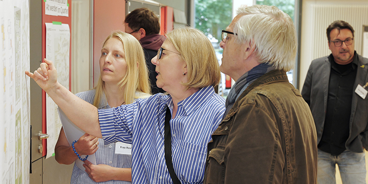 Teilnehmende der Bürgerversammlung stehen vor Metaplanwänden und besprechen in Gruppenarbeit ihre Wünsche, Anregungen und Bedenken zu verschiedenen Themen.